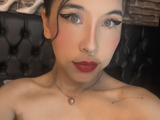 SofiBrandford has red lipstick, black winged eyeliner, a nose ring, and a heart necklace. Her bare shoulders show a small tattoo on her right side.