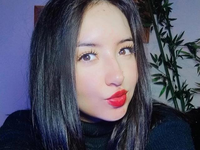 SusanMonroy has shiny black hair, brown eyes, and bright red lipstick. She's making a pouty face, looking slightly to the side with long, fake eyelashes.