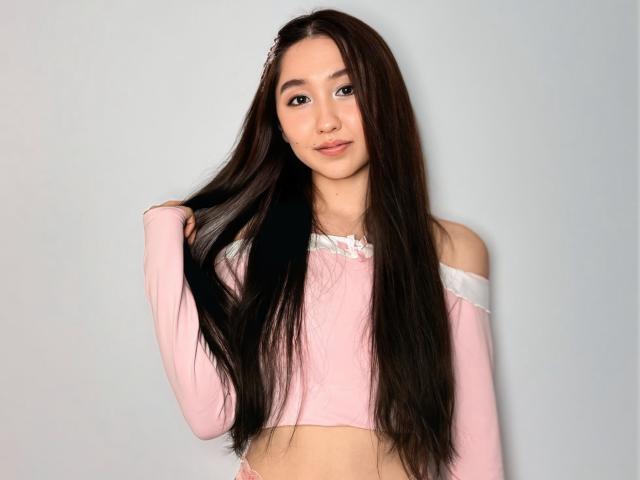 AddaDi with long brown hair, pink off-shoulder top, holding hair, cute face, small tits, light skin, standing, smiling, soft lighting, simple background, casual, cute, sexy.