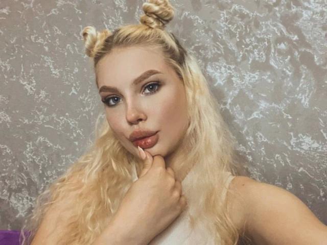 Blonde Byanka-hot with double braids, blue eyes, and glossy lips, biting her finger, has a sexy, cute face, and is wearing a white top. Her tits are not visible.