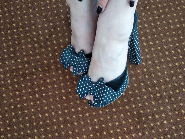 Nurri's feet in blue polka dot high heels with bow details, white socks, black painted toenails, standing on brown carpet with yellow dots.