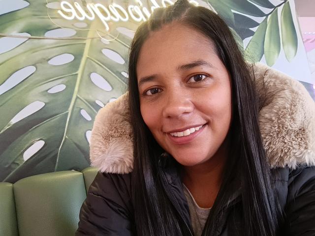 PauletteLoveX has dark brown skin, long straight black hair, and a cute smile. She's wearing a black puffy jacket with a furry hood. Boobs are not visible.