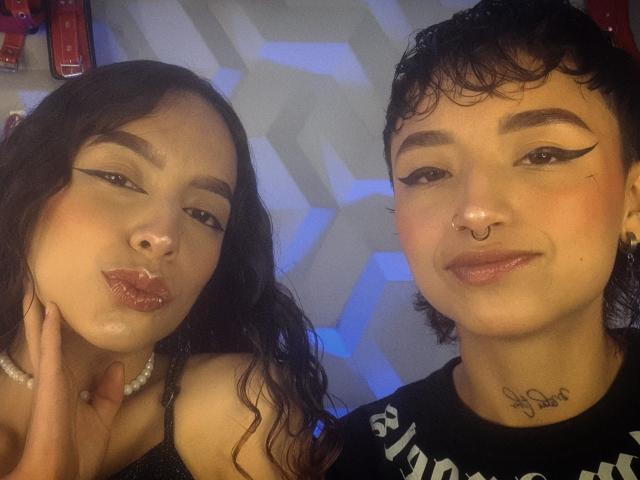 RileyAndAlexa have puffy lips with white substance on them, wearing makeup with thick eyeliner, a nose ring, and a tattoo under their chins. RileyAndAlexa's dark hair is wavy.