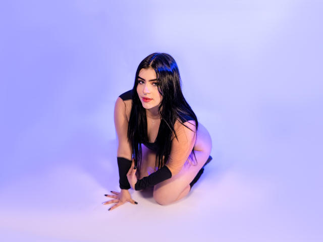 VynxDarkFire on all fours, wearing a black top, black gloves, and black boots, with long black hair and a cute, sexy face, looking at the camera.