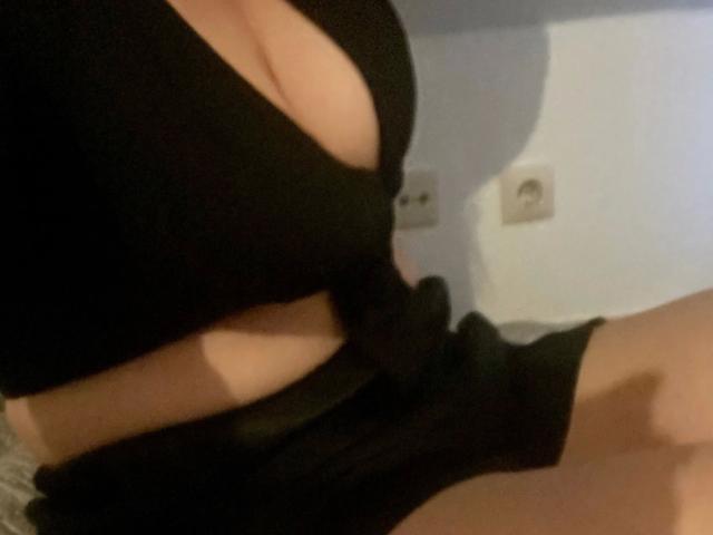 Kathinka-hot's big, curvy tits in a tight black top, showing a lot of cleavage and a side view of her black skirt and bare, tan skin.