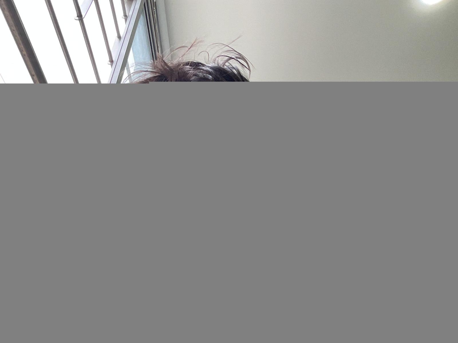 Sandvelvet's messy brown hair peeks over a gray wall, with sunlight from a window casting a bright reflection on the white ceiling above.