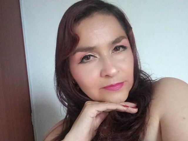 YaraStone ha i capelli castano scuro, l'ombretto rosa e il rossetto rosa. Ha il mento appoggiato sulla mano e guarda la fotocamera con un leggero sorriso..