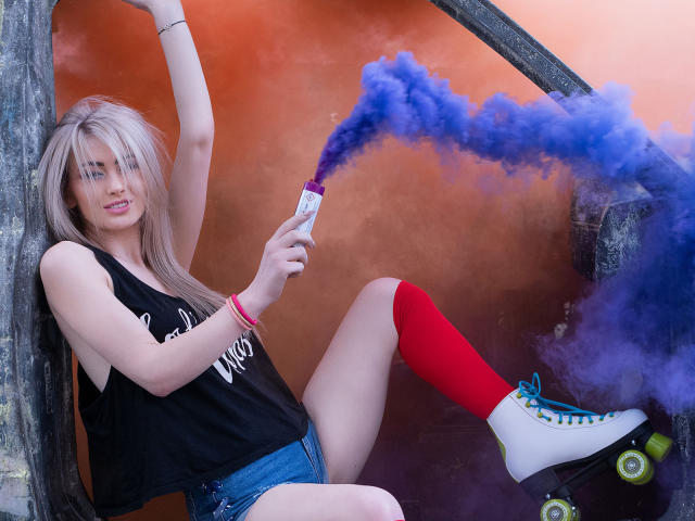 LindaBryns with blonde hair, wearing a black tank top, red knee socks, and white roller skates, smoking blue smoke from a vape, leaning against a tree.
