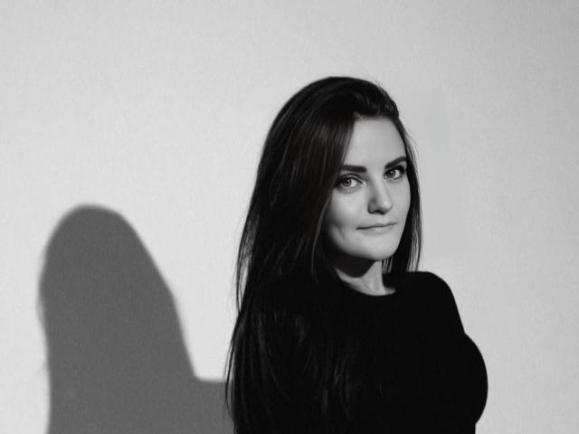 FortuneMiranda with long dark hair, shadow on the wall, wearing a black top, looking to the side with a slight smile, black and white photo.