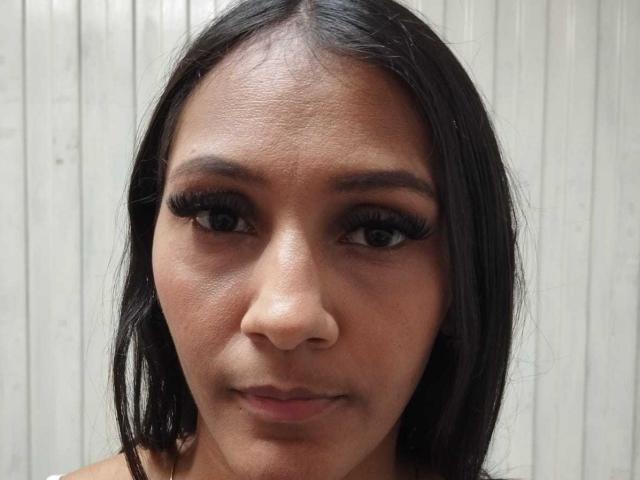 CarameloaPasionada has dark brown eyes, long black eyelashes, straight black hair, and a smooth brown skin tone with a slight sheen. Her nose is small and her lips are slightly closed.