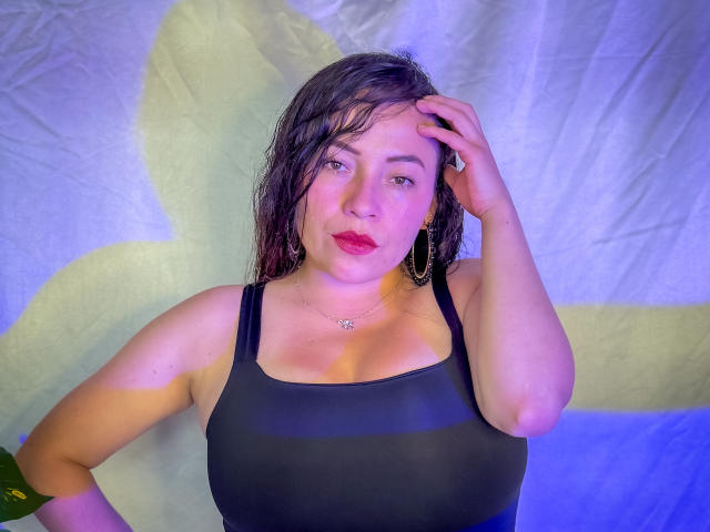 HoneyHotX with wet black tank top, medium tits, hand in hair, blue-purple light, green earrings, subtle makeup, slight smile, white background, casual pose, slightly sweaty skin.