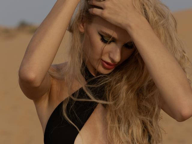 FloraDavis with blonde hair, black halter top, eyes closed, hands in hair, soft sunlight, slight smile, sandy background, long wavy hair, subtle makeup, gentle expression, sexy.