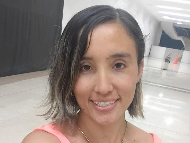 HinataLove has medium-length, wet black hair with gray tips, brown eyes, and a slight smile showing metal braces. She wears a pink top and a gold necklace.