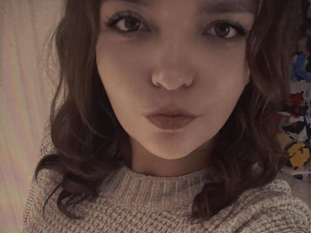 NettyKisyla has brown wavy hair, a nose ring, and is wearing a knitted sweater. She's staring into the camera with pouty lips and thick, dark eyelashes.