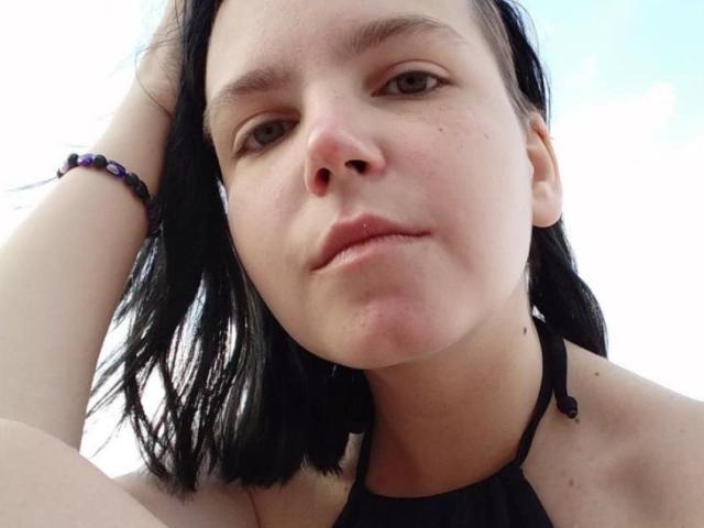 SpicyDora's face, black hair, light skin, subtle pout, no makeup, black halter top, purple bead bracelet on right wrist, hand in hair, slightly blurred, outdoors.