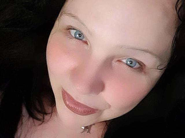 Blackbeauty43-hot's face, pale with blue eyes, black hair, and pink lips, smiling slightly, wearing a silver necklace. She has a cute, sexy, and attractive look.