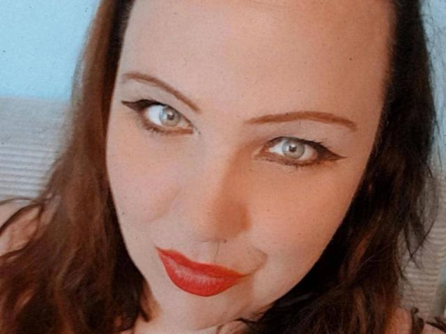 Blackbeauty43-hot has pale skin, blue eyes, and red lipstick. She's smiling with dark brown hair, black eyeliner, and a nose piercing. Boobs are not visible.