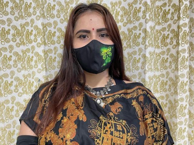 DaliaDubey with brown hair, black mask with green leaf design, black and gold ornate top, and necklace, looking at camera. She's wearing a red bindi.