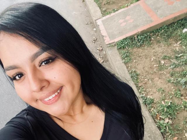 TindraZavaleta has long black hair, brown eyes, and a cute smile with her lips slightly parted. She's wearing a black top, and her skin is light brown.