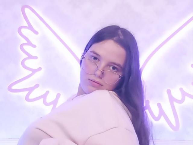 SophieDreams with long brown hair, wearing glasses and a white sweater, has a cute face and soft expression, neon pink angel wings in the background.