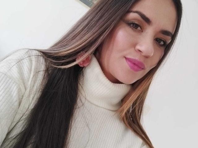 TheresaLarson with long brown hair, pink lipstick, white turtleneck, and subtle makeup, smiling slightly, looking at the camera, has a cute face and small ass.