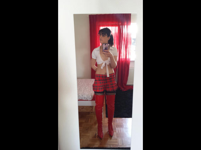 sweetSilvana-hot with red plaid skirt, white tied crop top, and red thigh-high boots, taking a mirror selfie, showing her ass and red pointed heels.