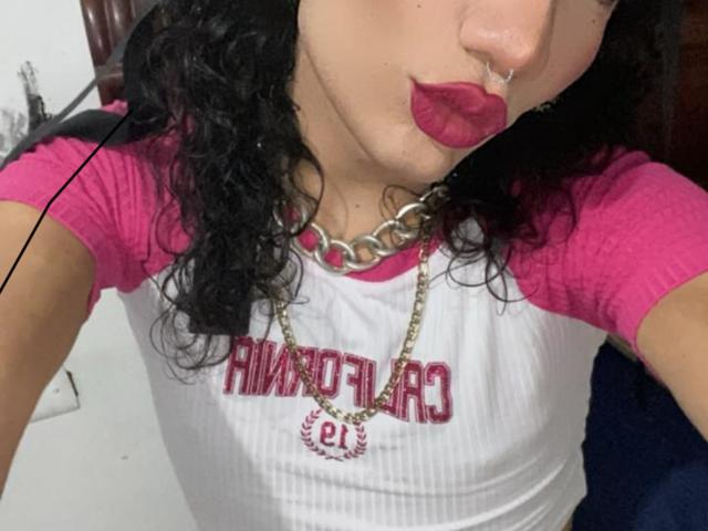 SweetSamyPrincipal with curly black hair, pink rag tee, and white shirt, pouty pink lips, silver nose ring, gold chain necklace, pink lipstick, and a hot face.