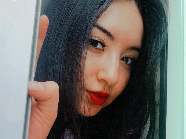 SusanMonroy's face with long black hair, red lipstick, and nose piercing, holding a door frame, showing off her red-ass lips and dark-ass eyes, looking sexy.
