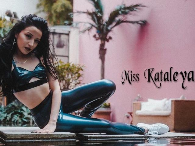 MissKataleya-hot with long black hair, wearing a shiny black latex crop top and matching high-waisted leggings, sitting on a stone surface in white sneakers, showing her ass.
