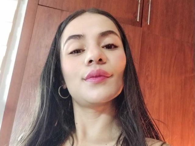 OshumBae has long black hair, brown eyes, and pink lipstick, with a small nose and hoop earrings, smiling slightly at the camera.
