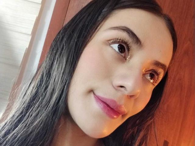 OshumBae has long black hair, brown eyes, and pink lipstick with a slight smile. Her face is slightly angled to the right. Her nose is small and her skin is light.