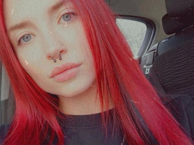CherrySmarry-hot with red hair, blue eyes, and a nose ring, wearing a black shirt, sitting in a car, showing a calm, neutral expression.