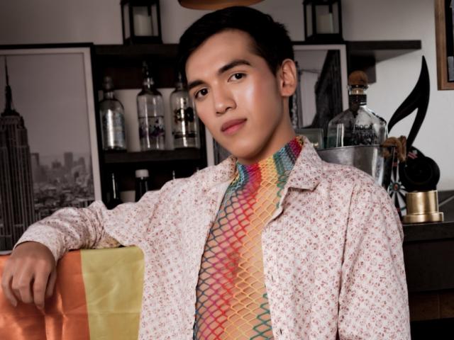 TheoBlake, Asian dude with short black hair, wearing a floral shirt and colorful, patterned necktie, leaning on a yellow-orange bag, looking at camera with a slight smile.