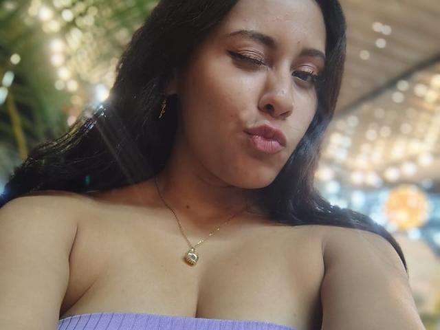 MarilynHills, puffy lips, brown eyes, long black hair, purple tube top, small gold necklace, visible cleavage, slightly tanned skin, subtle makeup, bokeh background.