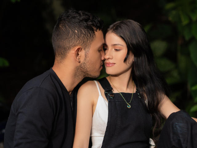 EimyAndMaxi with dark hair, white tank top, and black denim dress, kissed on the cheek by EimyAndMaxi with short hair, black shirt, and gold necklace.