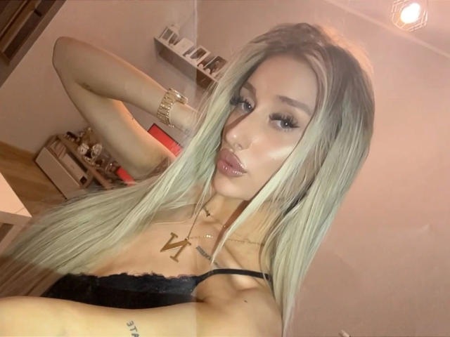 NatalieSusse-hot with long blonde hair, pouty pink lips, gold necklace, black lace top, and gold bracelet, looking at the camera with a sexy, confident expression.