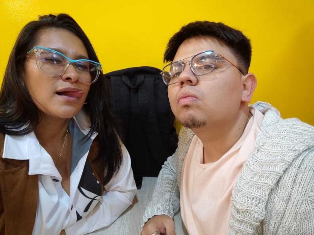 JuliaxRosee with brown skin, black hair, blue glasses, white shirt, brown vest, and JuliaxRosee with tan skin, black hair, clear glasses, gray sweater, pink shirt, pouting.
