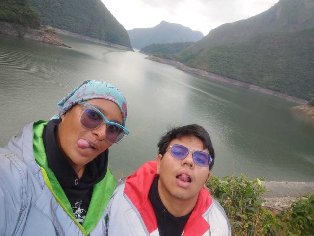 JuliaxRosee with a blue headscarf and blue sunglasses, sticking out tongue. JuliaxRosee next to her, with black hair, red and white jacket, and blue sunglasses, sticking out tongue.