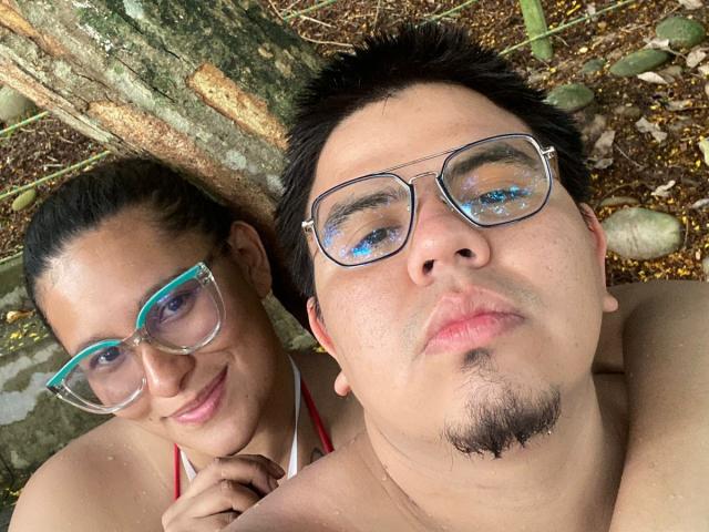 JuliaxRosee with glasses, blue frames, and a smile, next to a shirtless JuliaxRosee with glasses, metal frames, and a slight mustache, lying under a tree.