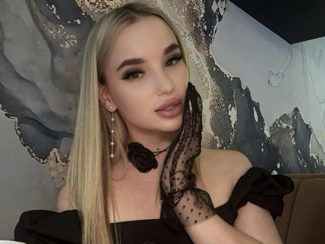 KiraKrox has blonde hair, wearing an off-shoulder black dress, polka-dot glove, and rose choker, with makeup and earrings, looking sexy with pouty lips.