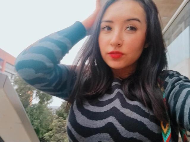 SusanMonroy, com cabelo escuro, vestindo um suéter listrado preto e cinza, batom vermelho, com a mão no cabelo, olhando para a câmera, tamanho médio de seios, luz suave, ligeiramente borrada..