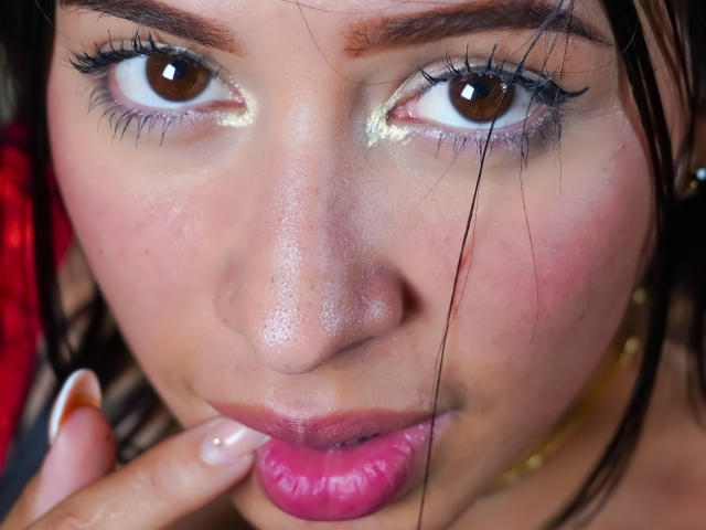 Ciamsth's face, brown eyes, pink glossy lips, slightly parted, gold shimmer on eyelids, dark brown eyebrows, finger gently touching bottom lip, short brown hair, subtle skin texture.