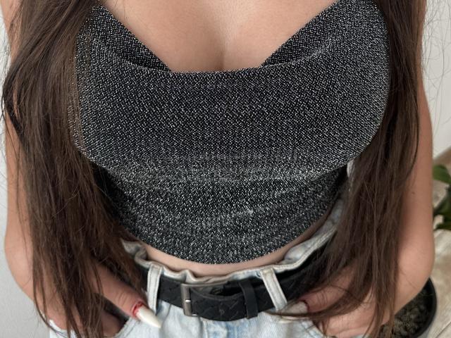 KrisTeigen's sparkly black crop top with a deep V-neck, showing her small, firm tits. Her hands are on her jeans, with long brown hair on both sides.