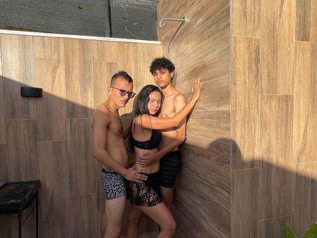 Three WorldSexxxADS standing in a wooden-tiled shower. One with glasses and zebra shorts, one with curly hair and black shorts, one with black lingerie, all touching.