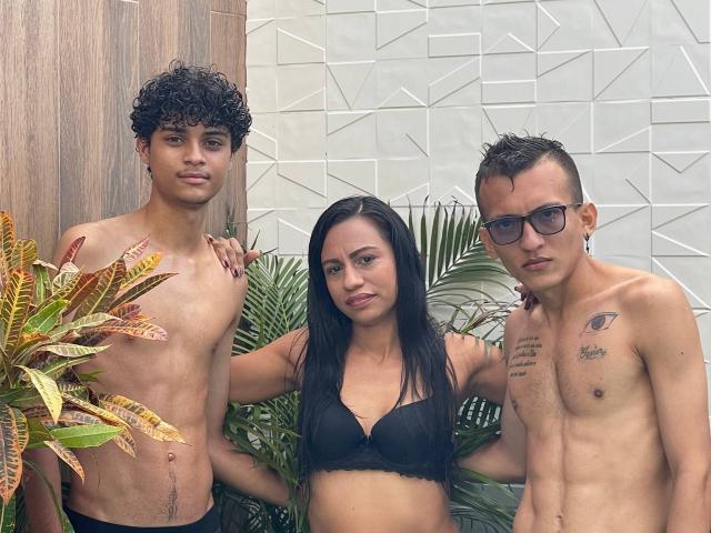Three WorldSexxxADS: curly-haired dude with small tits, black-haired chick with boobs in black bra, and dude with tattoos and glasses, all shirtless, standing in front of plants.
