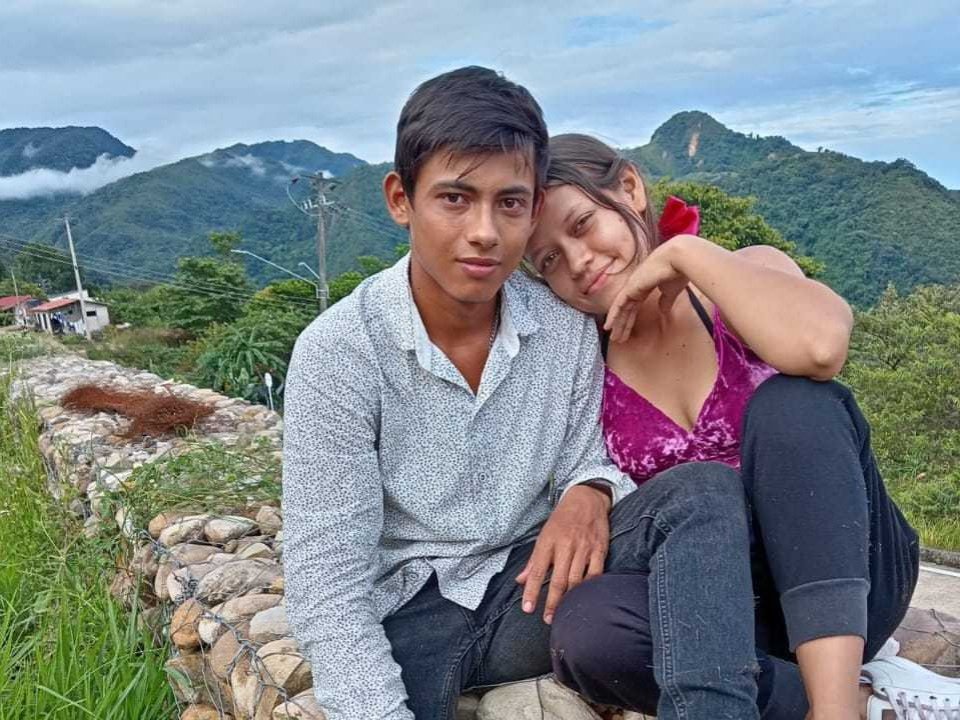 FantasyasCompartidas69, with short black hair and a grey shirt, sits beside FantasyasCompartidas69, who has brown hair, a pink top, and black pants, resting her head on his shoulder.