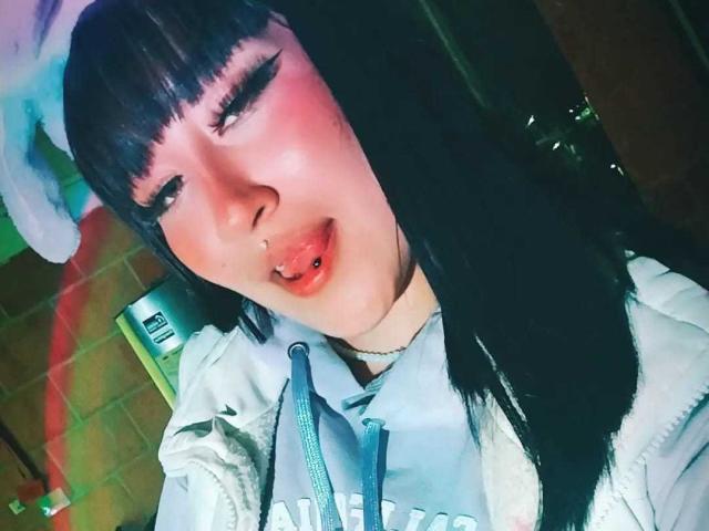 SydneySweetX heeft zwart haar, een pony en een neuspiercing met een lipiercing. Ze draagt een witte hoodie, een blauwe band en heeft roze blush en donkere eyeliner..