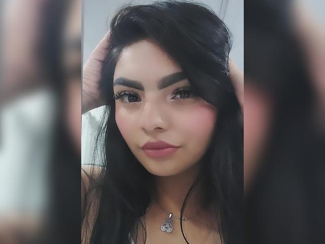 CarlaFiorell ha i capelli scuri e mossi, sopracciglia folte, guance rosate e labbra piene. Si sta guardando allo specchio, con una mano tra i capelli, e indossa una collana..