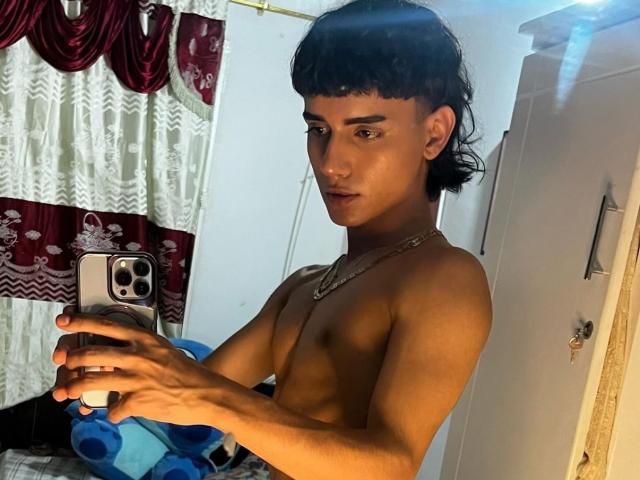 IvyMiller, shirtless, with dark hair, taking a mirror selfie with a phone, showing off a slim, toned, tan body, and wearing a necklace. Blue stuffed toy in the background.