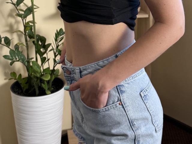 Stefanni's midriff in light blue denim shorts with her hand in the pocket, wearing a black cropped top, showing a slight tan and her blue-painted nails.